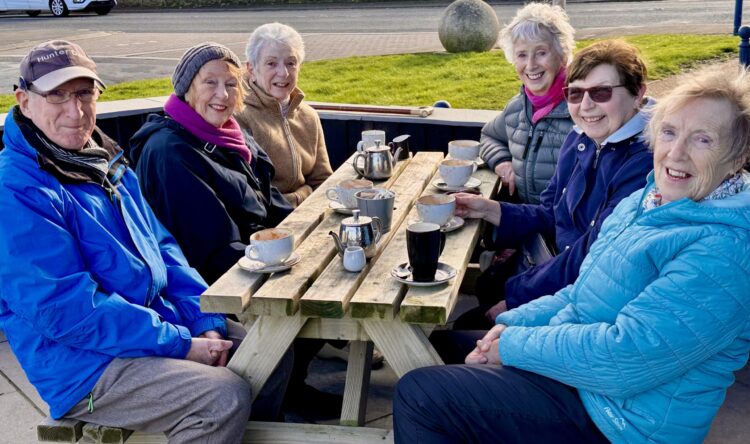 Strollers sitting at a picnic table having a coffee